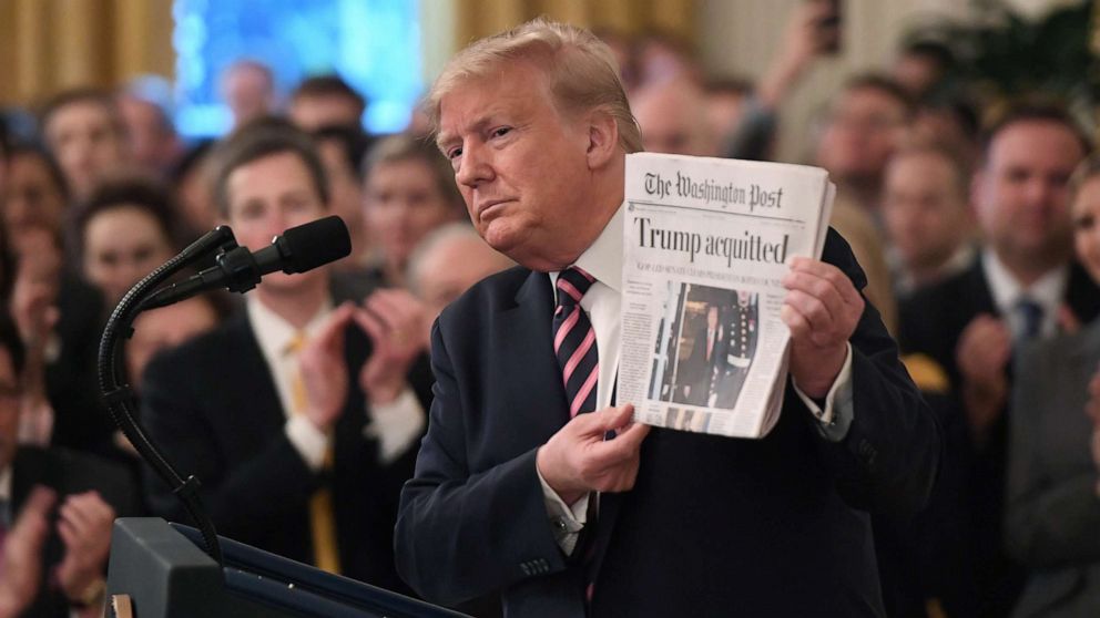 PHOTO: President Donald Trump holds up a newspaper that displays a headline "Acquitted"  while peaking about his Senate impeachment trial in the East Room of the White House, Feb. 6, 2020.