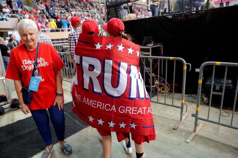 PHOTO: Lori Broughton, right, and Lydia Roy, both of Lafayette, La., walk through the arena wrapped in a Trump campaign flag, before President Donald Trump arrives to speak at a campaign rally in Lake Charles, La., Oct. 11, 2019.