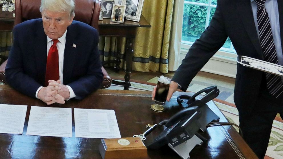PHOTO: An unidentified valet places a glass of soda on President Donald Trump's desk as he engages in an interview with Reuters during the coronavirus disease (COVID-19) response at the White House, April 29, 2020.