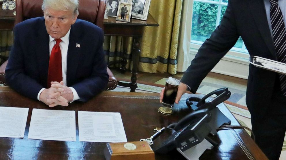 PHOTO: An unidentified valet places a glass of soda on President Donald Trump's desk as he engages in an interview with Reuters during the coronavirus disease (COVID-19) response at the White House, April 29, 2020.