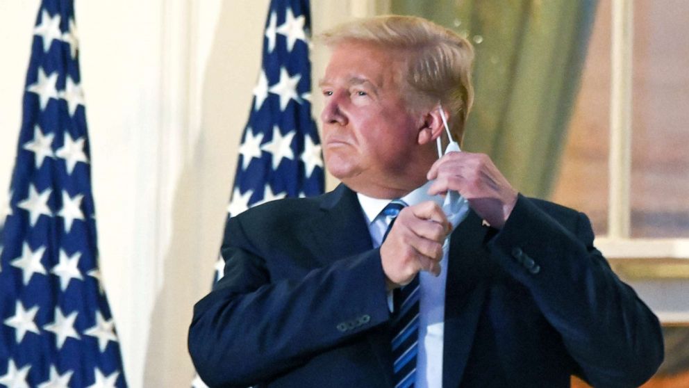 PHOTO: President Donald Trump pulls off his protective face mask as he poses atop the Truman Balcony of the White House after returning from being hospitalized at Walter Reed Medical Center for coronavirus disease (COVID-19) treatment, Oct. 5, 2020. 