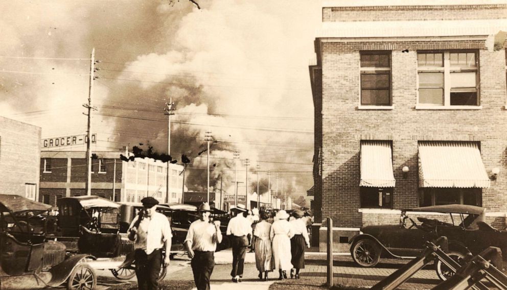 PHOTO: Two armed men walk away from burning buildings as others walk in the opposite direction during the Tulsa Race Massacre in Tulsa, Okla. June 1, 1921. 
