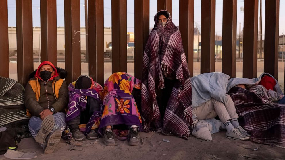 PHOTO: Immigrants bundle up against the cold after spending the night outside along the U.S.-Mexico border fence on Dec. 22, 2022, in El Paso, Texas.