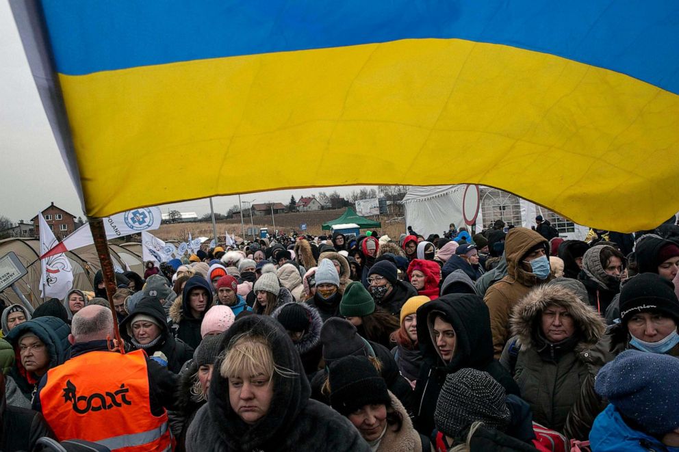 PHOTO: FILE - A Ukrainian volunteer holds a Ukrainian flag and directs hundreds of refugees after fleeing from the Ukraine and arriving at the border crossing in Medyka, Poland, March 7, 2022.