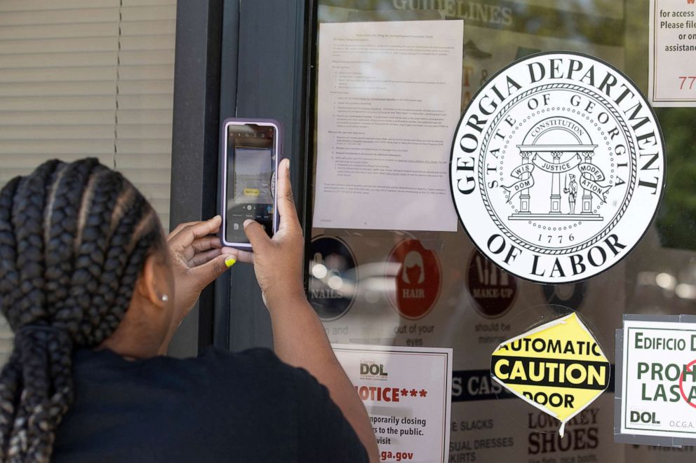 PHOTO: Arnashia McCain uses her phone to copy phone numbers posted on the locked doors of a Georgia Department of Labor office, May 7, 2020, in Norcross Ga. McCain drives for Lyft and has been unable check on the status of her her unemployment claim.