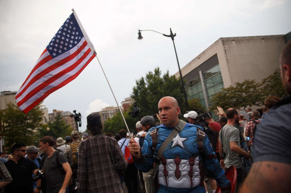 PHOTO: A counterprotester dressed as Captain America taunts white supremacists, escorted by police, who are making their way from Foggy Bottom Metro station to Lafayette Park for a "Unite the Right" event on Aug. 12, 2018, in Washington, D.C.