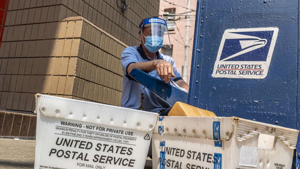 PHOTO: A U.S. Postal Service worker wearing a protective mask and face shield removes mail from a dropbox in San Francisco, Calif., Aug. 17, 2020. 