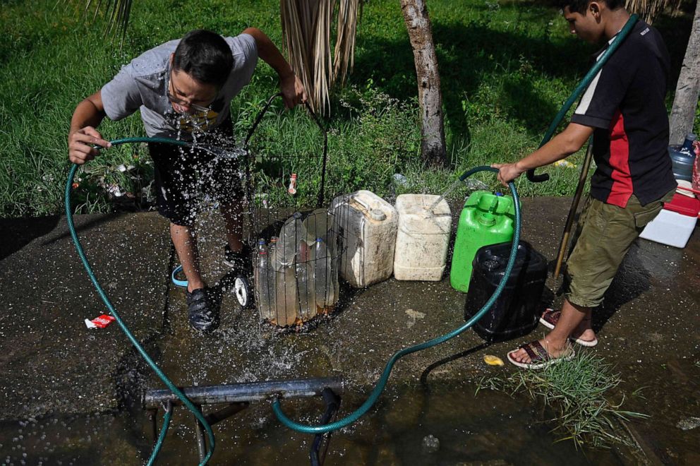 PHOTO: A boy drinks water as another fills cans from a makeshift intake set on a sidewalk for people to collect water in Maracaibo, Zulia State, Venezuela, on July 23, 2019.