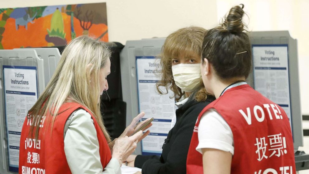 PHOTO: Poll workers speak to a woman wearing a face mask in a polling site at San Francisco City Hall on Super Tuesday, March 3, 2020, in San Francisco.