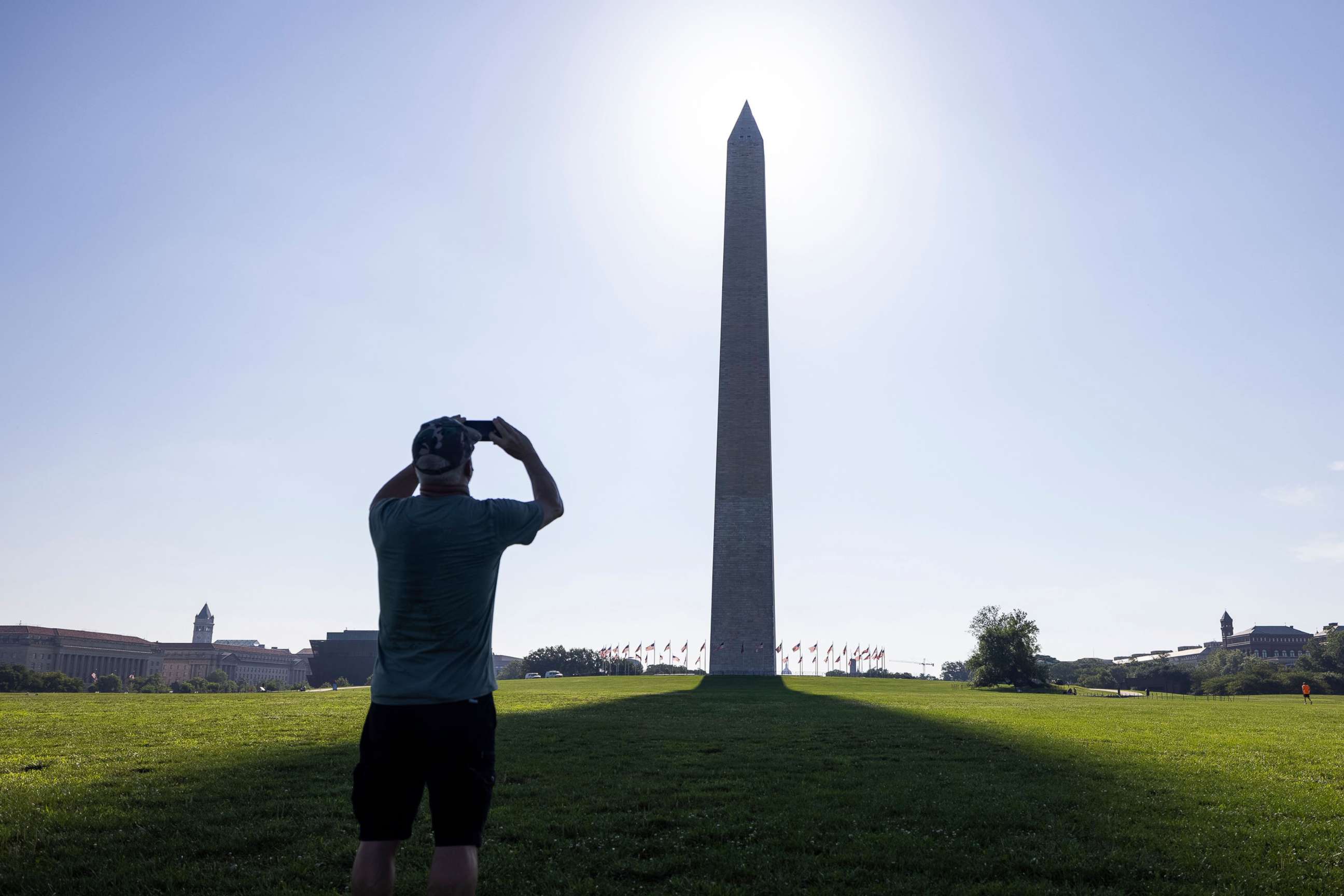 PHOTO: A man takes photographs while standing in the shadow cast by The Washington Monument in Washington, D.C., July 13, 2021. 