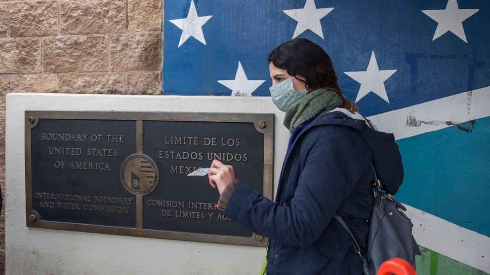 PHOTO: A young woman with a mouth guard shows her visa at the border crossing between Tijuana and the US, March 17, 2020.