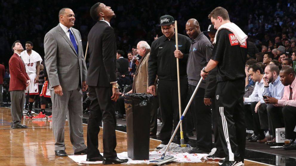 Brooklyn Nets head coach Lionel Hollins, left, stands beside floor attendants as a roof leak causes a delay in the first half of their NBA basketball game against the Miami Heat at the Barclays Center, Dec. 16, 2014, in New York.
