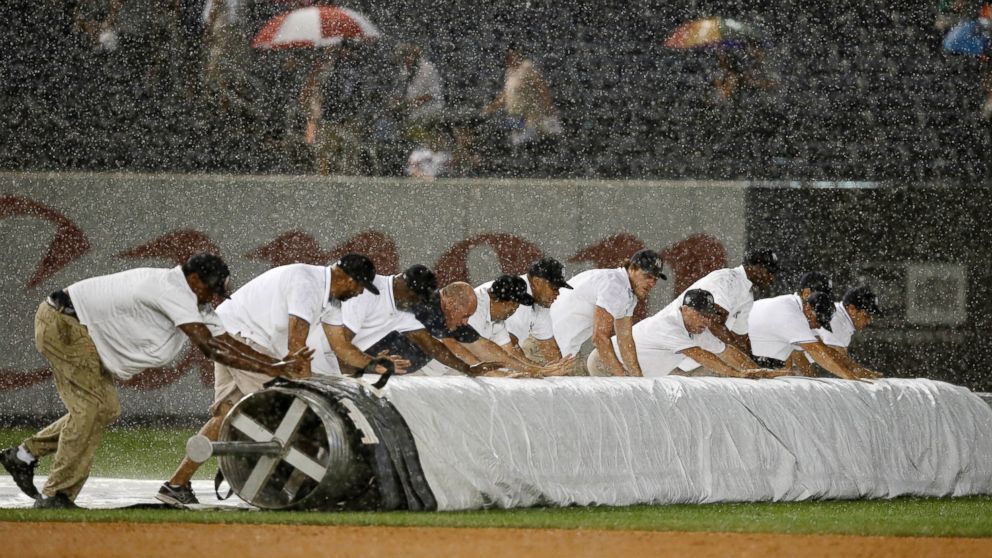 PHOTO: Grounds crew members unroll the tarp during a rainstorm in the fifth inning of a baseball game between the Texas Rangers and the New York Yankees at Yankee Stadium in New York, July 23, 2014.