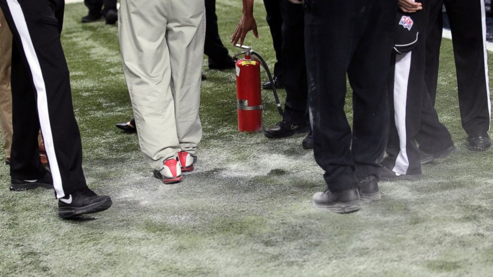 Workers and officials stand over a section of charred turf burned during pyrotechnics before an NFL football game between the St. Louis Rams and the Pittsburgh Steelers on Sept. 27, 2015, in St. Louis.