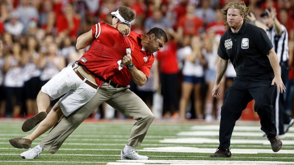 Ohio State strength and conditioning coach Anthony Schlegel tackles a person who ran onto the field during the second quarter of the NCAA college football game between Ohio State, Sept. 27, 2014, in Columbus, Ohio. 