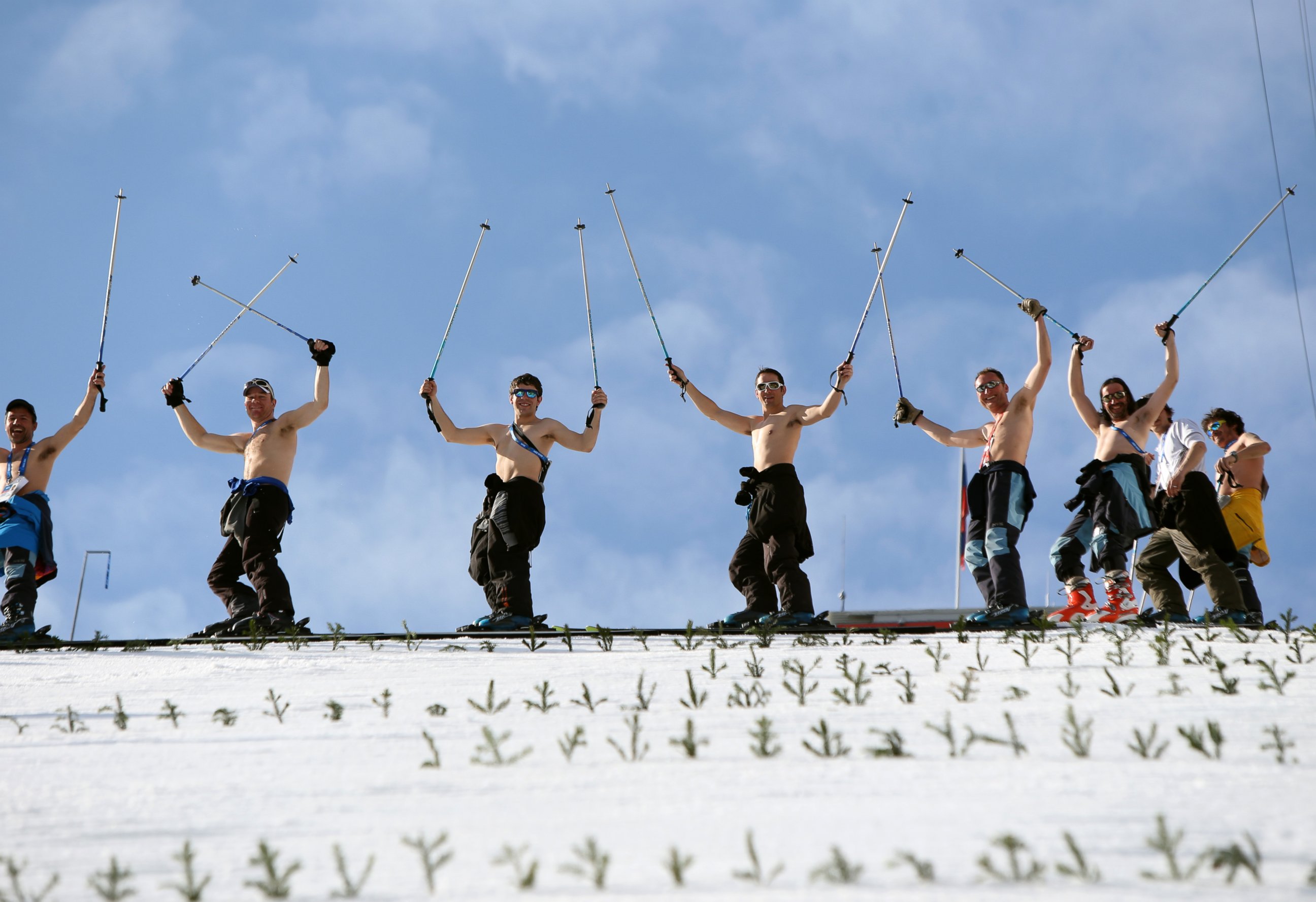PHOTO:Course workers take off their shirts to enjoy the warm weather as they prepare the landing hill before the men's Nordic combined normal hill training jump at the RusSki Gorki Jump Center at the 2014 Sochi Winter Olympics.