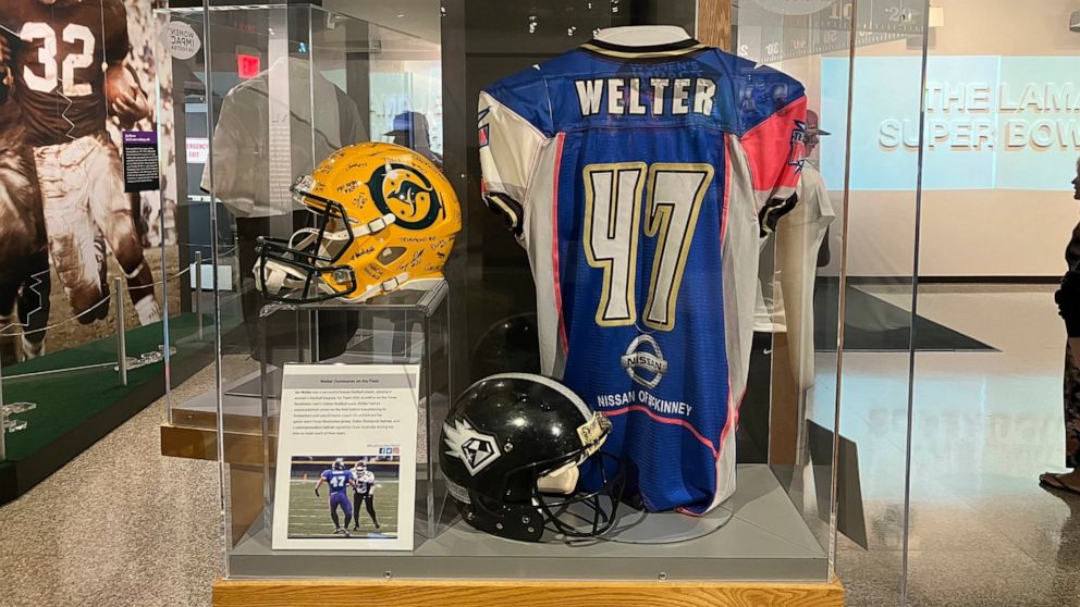 This photo shows a display with Jen Welter's blue-and-pink jersey, Friday, Aug. 5, 2022 in Canton, Ohio. A 15-year-old boy made his way through the The Pro Football Hall of Fame museum on Friday, checking out the memorabilia and bronze busts before s