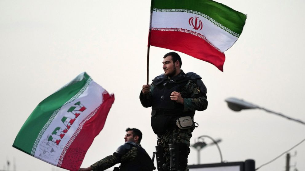 Two anti-riot police officers wave the Iranian flags during a street celebration after Iran defeated Wales in Qatar's World Cup, at Sadeghieh Sq. in Tehran, Iran, Friday, Nov. 25, 2022. Iran's political turmoil has cast a shadow over Iran's matches a