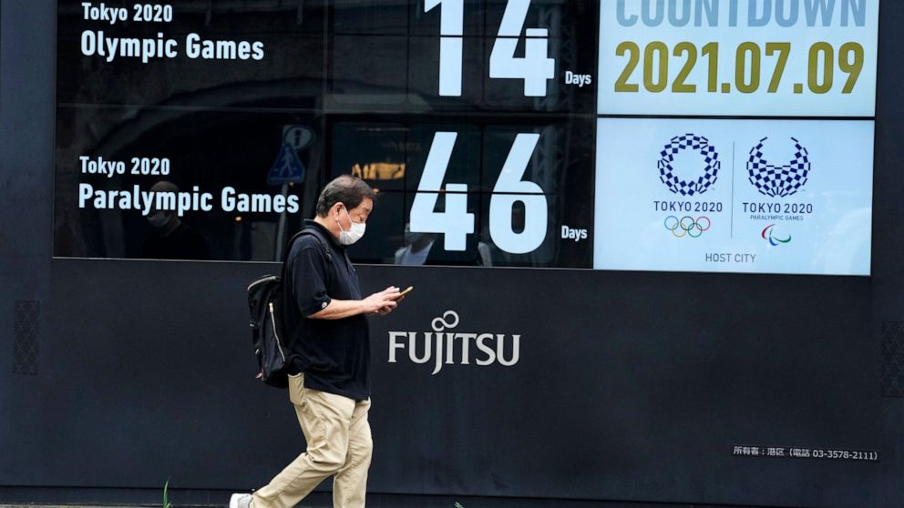 A man wearing a face mask walks past the countdown clock for the Tokyo 2020 Olympic and Paralympic Games near the Shimbashi station, Friday, July 9, 2021, in Tokyo. (AP Photo/Eugene Hoshiko)