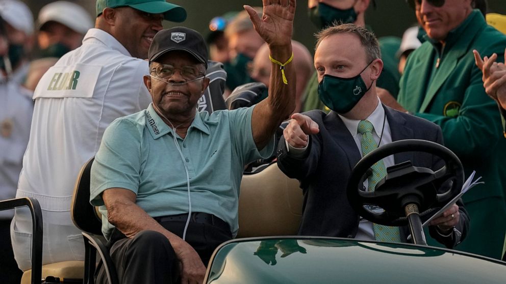 FILE - Lee Elder waves as he arrives for the ceremonial tee shots before the first round of the Masters golf tournament on Thursday, April 8, 2021, in Augusta, Ga. At far right is Phil Mickelson. Person at right in cart is unidentified. Elder broke d