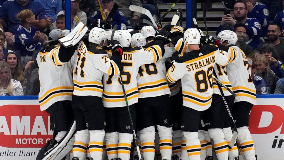 Boston Bruins players mob center Patrice Bergeron after Bergeron assisted on a goal by left wing Brad Marchand for his 1,000th career point against the Tampa Bay Lightning during the second period of an NHL hockey game Monday, Nov. 21, 2022, in Tampa