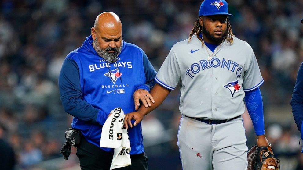 A trainer helps Toronto Blue Jays first baseman Vladimir Guerrero Jr., who injured his hand during the second inning of the team's baseball game against the New York Yankees on Wednesday, April 13, 2022, in New York. (AP Photo/Frank Franklin II)