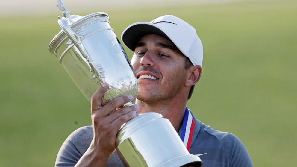 FILE- In this June 17, 2018, file photo Brooks Koepka holds up the Golf Champion Trophy after winning the U.S. Open Golf Championship in Southampton, N.Y. Koepka says the key to victory were 9-irons he hit on the 16th and 17th holes of the final roun