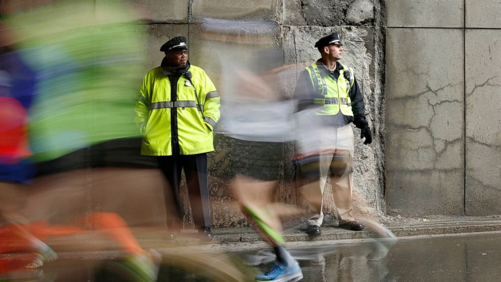 FILE - Police officers stand watch as Boston Marathon runners race along the course, April 20, 2015, in Boston. The Boston Marathon returns to the traditional Patriots Day holiday, Monday, April 18, 2022, for the first time in three years, and runner