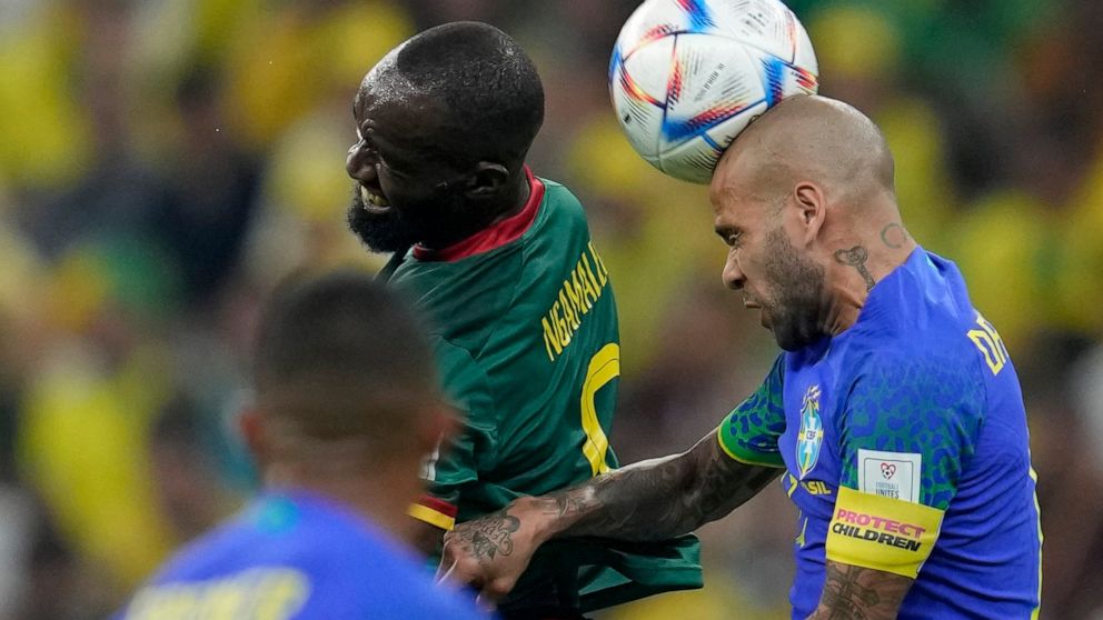 Brazil's Dani Alves, right, heads the ball past Cameroon's Moumi Ngamaleu during the World Cup group G soccer match between Cameroon and Brazil, at the Lusail Stadium in Lusail, Qatar, Friday, Dec. 2, 2022. (AP Photo/Natacha Pisarenko)