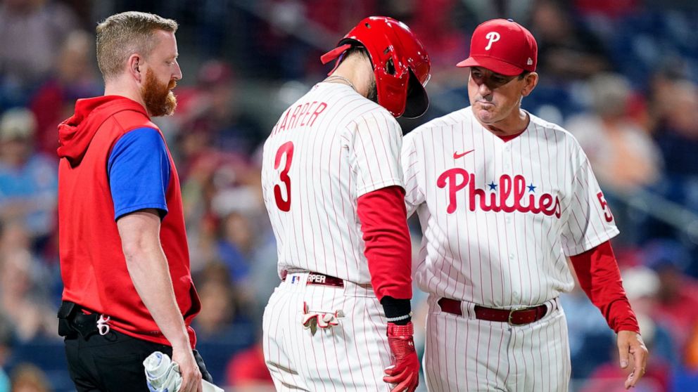 Philadelphia Phillies' Bryce Harper, center, is checked on by interim manager Rob Thomson, right, during the sixth inning of a baseball game against the Miami Marlins, Wednesday, Sept. 7, 2022, in Philadelphia. (AP Photo/Matt Slocum)