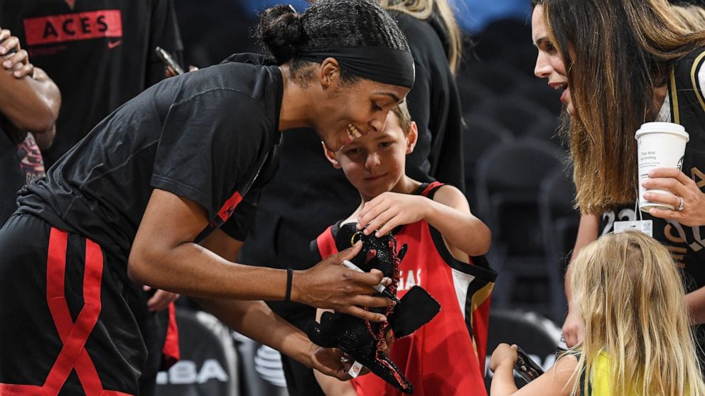 Las Vegas Aces guard Sydney Colson, left, autographs a stuffed animal for Calvin Heuer, center, as his mother Megan Heuer, upper right, looks on before a WNBA basketball game against the Seattle Storm, Sunday, Aug. 14, 2022, in Las Vegas. (AP Photo/S