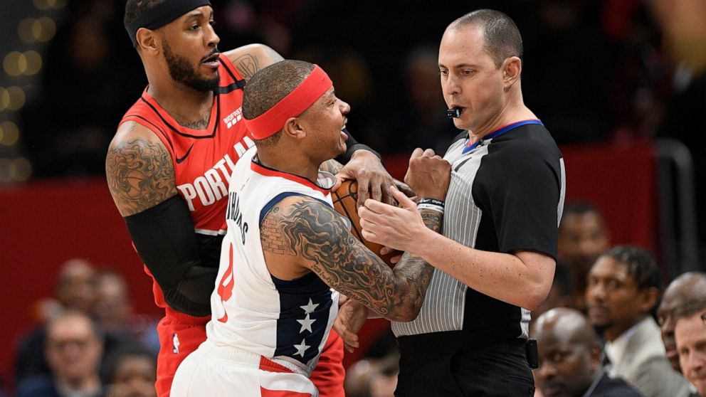 Washington Wizards guard Isaiah Thomas (4) comes in contact with referee Marat Kogut, right, next to Portland Trail Blazers forward Carmelo Anthony, back, during the first half of an NBA basketball game, Friday, Jan. 3, 2020, in Washington. Thomas wa