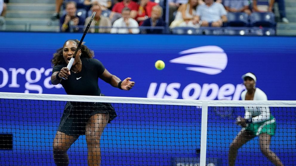 Serena Williams, left, returns a shot as Venus Williams, of the United States, looks on during their first-round doubles match against Lucie Hradecká and Linda Nosková, of the Czech Republic, at the U.S. Open tennis championships, Thursday, Sept. 1, 