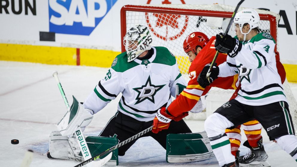 Dallas Stars goalie Jake Oettinger, left, kicks the puck away from Calgary Flames left wing Milan Lucic, center, as Flames' Miro Heiskanen defends during the second period of Game 2 of an NHL hockey Stanley Cup first-round playoff series in Calgary, 