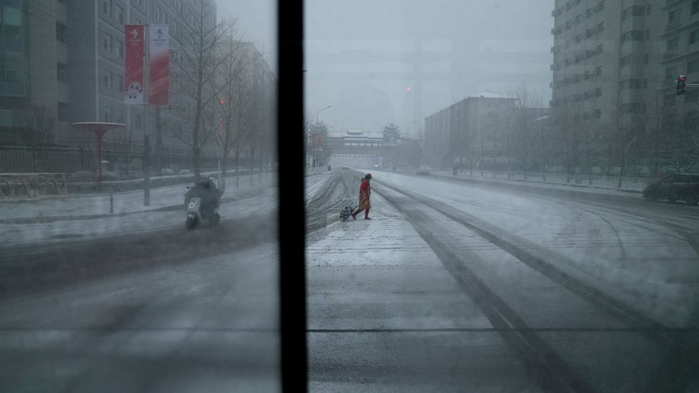A woman crosses a street, seen from a window bus, at the 2022 Winter Olympics, Sunday, Feb. 13, 2022, in Beijing. (AP Photo/Natacha Pisarenko)