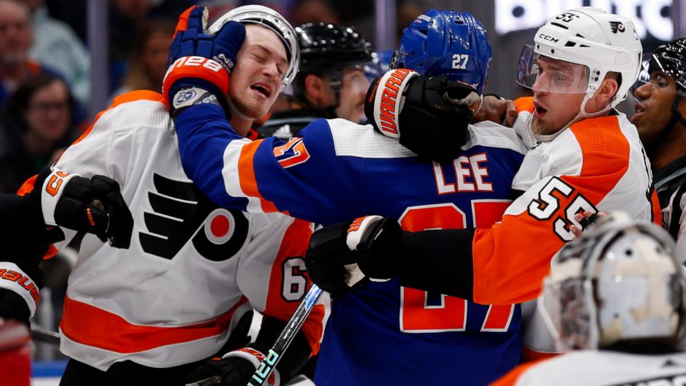 New York Islanders left wing Anders Lee (27) hits Philadelphia Flyers defenseman Travis Sanheim (6) while being restrained by Flyers defenseman Rasmus Ristolainen (55) during the second period of an NHL hockey game Saturday, Nov. 26, 2022, in Elmont,