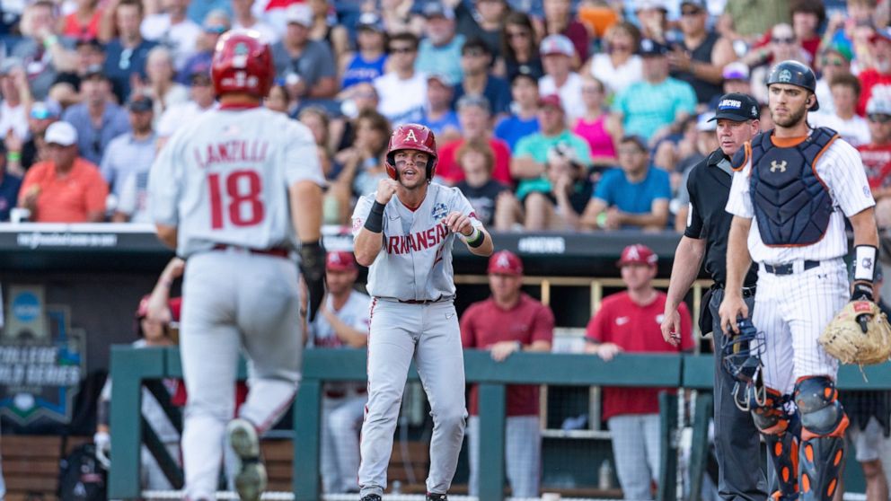 Arkansas' Michael Turner (12) scores and cheers on Chris Lanzilli (18) running home for a second run against Auburn in the third inning during an NCAA College World Series baseball game Tuesday, June 21, 2022, in Omaha, Neb. (AP Photo/John Peterson)