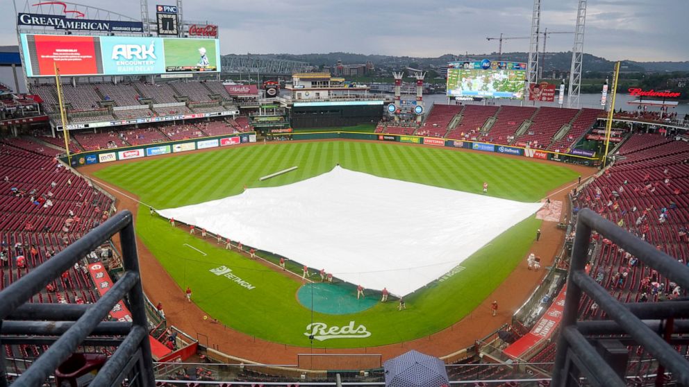 Grounds crew members lay a tarp over the infield prior to a baseball game between the Colorado Rockies and the Cincinnati Reds, Saturday, Sept. 3, 2022, in Cincinnati. (AP Photo/Jeff Dean)