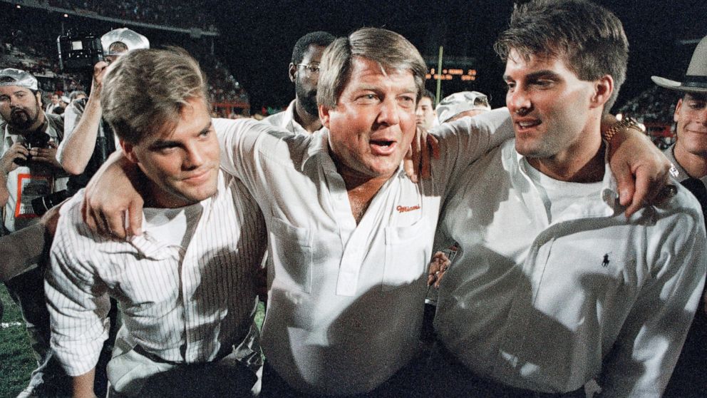 FILE - Miami coach Jimmy Johnson, center, is hugged by his sons, Chad, left, and Brent, rightk, while walking off the field following the team's win over Nebraska in the Orange Bowl college football game in Miami, Jan. 2, 1989. Johnson won two Super 