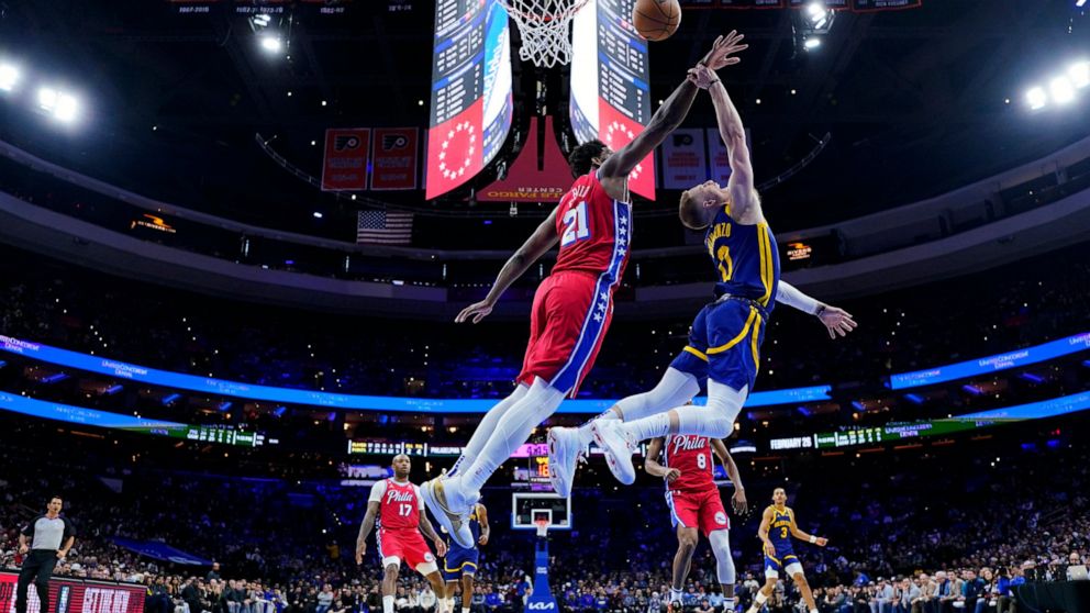 Golden State Warriors' Donte DiVincenzo, right, tries to get a shot past Philadelphia 76ers' Joel Embiid during the second half of an NBA basketball game, Friday, Dec. 16, 2022, in Philadelphia. (AP Photo/Matt Slocum)
