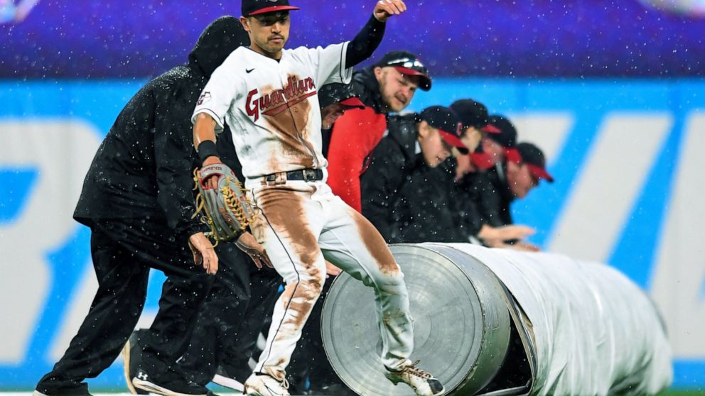 Cleveland Guardians' Steven Kwan avoids the grounds crew rolling out a tarp during a rain delay in the fifth inning of the team's baseball game against the Texas Rangers, Wednesday, June 8, 2022, in Cleveland. (AP Photo/Nick Cammett)