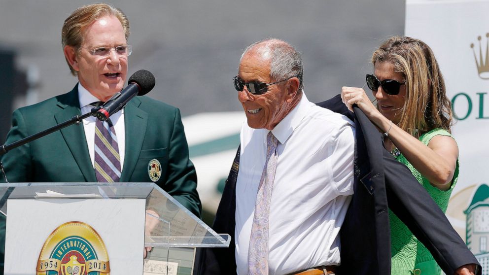 FILE - Monica Seles, right, helps Nick Bollettieri with a blazer as Hall of Fame chairman of the board Christopher Clouser, left, looks on during Bollettieri's induction into the International Tennis Hall of Fame in Newport, R.I., Saturday, July 12, 