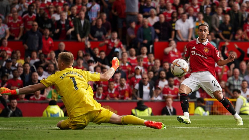Manchester United's Antony, right, scores his side's opening goal past Arsenal's goalkeeper Aaron Ramsdale during the English Premier League soccer match between Manchester United and Arsenal at Old Trafford stadium, in Manchester, England, Sunday, S