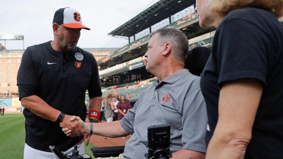Baltimore Orioles manager Brandon Hyde, left, talks with former Orioles pitcher Jim Poole, center, and his wife, Kim Poole, prior to a baseball game against the Seattle Mariners, Thursday, June 2, 2022, in Baltimore. The Orioles honored Lou Gehrig Da