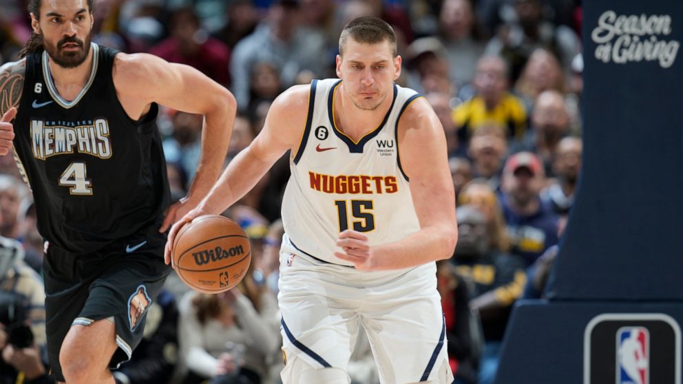Denver Nuggets center Nikola Jokic, front, picks up a loose ball as Memphis Grizzlies center Steven Adams pursues in the first half of an NBA basketball game Tuesday, Dec. 20, 2022, in Denver. (AP Photo/David Zalubowski)