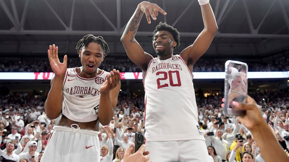 Arkansas players JD Notae, left), and Kamani Johnson (20) celebrate with fans after defeating Auburn 80-76 in overtime following an NCAA college basketball game Tuesday, Feb. 8, 2022, in Fayetteville, Ark. (AP Photo/Michael Woods)