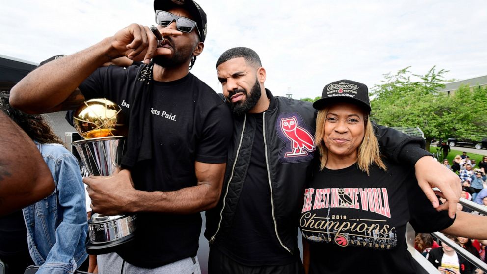Toronto Raptors forward Kawhi Leonard, left to right, smokes a cigar holding his playoffs MVP trophy as he celebrates with performing artist Drake and his mother Kim Robertson during the 2019 Toronto Raptors NBA basketball championship parade in Toro