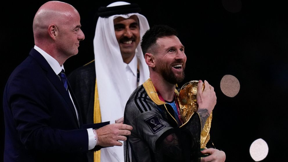 Argentina's Lionel Messi holds up the trophy flanked by FIFA President Gianni Infantino and The Emir of Qatar Sheikh Tamim bin Hamad Al Thani after winning the World Cup final soccer match between Argentina and France at the Lusail Stadium in Lusail,