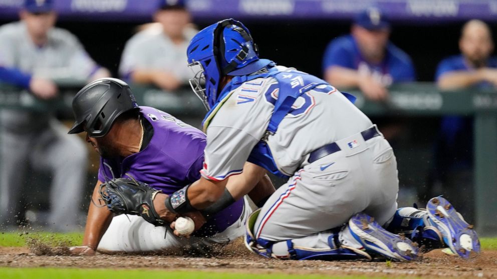 Texas Rangers catcher Meibrys Viloria, right, loses the ball after tagging out Colorado Rockies' Elias Diaz as he tries to score in the eighth inning of a baseball game Tuesday, Aug. 23, 2022, in Denver. (AP Photo/David Zalubowski)