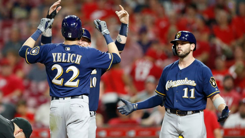 Milwaukee Brewers' Christian Yelich (22) is congratulated at the plate by Yasmani Grandal, obscured, left, and Mike Moustakas (11) following a two-run home run off Cincinnati Reds relief pitcher Robert Stephenson during the ninth inning of a baseball